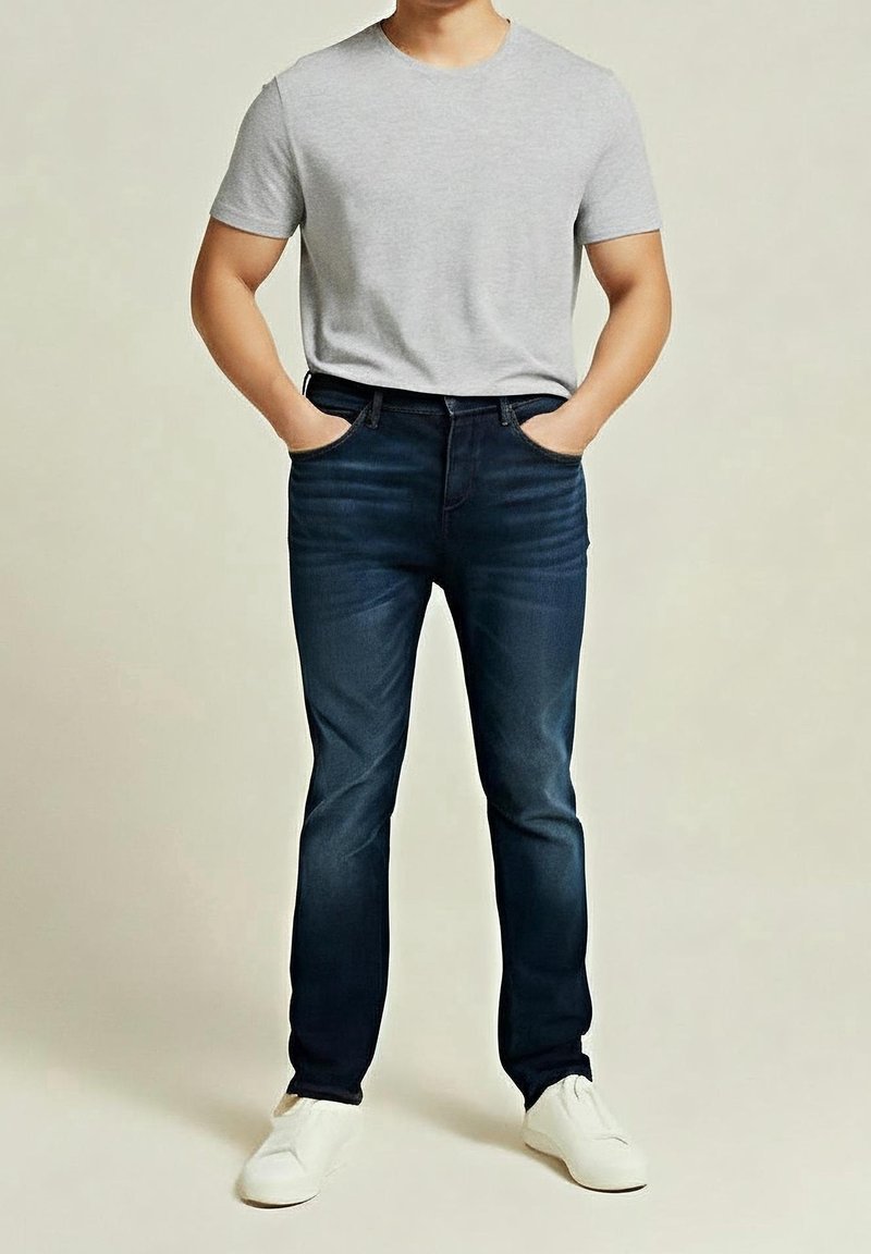 Camiseta de algodón gris combinada con jeans de mezclilla azul oscuro, diseño ajustado, con bolsillos, complementada con zapatos blancos. Atuendo simple y casual.
