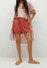 Leichte, gemusterte Hemd in Pink, beiger Tanktop, rostfarbene Shorts und beiger Sandalen mit Kreuzriemen. Glatte Texturen, lässiger Schnitt.