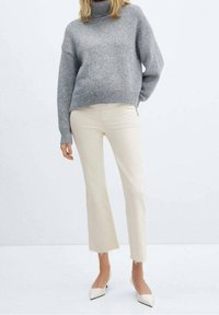 Jersey de tortuga gris claro combinado con pantalones cortos crema, con dobladillos sin rematar y tacones puntiagudos blancos.