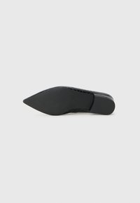 Chaussure noire à bout pointu avec une tige texturée, semelle en caoutchouc et un petit talon, présentant un design épuré sans embellissements ni motifs.