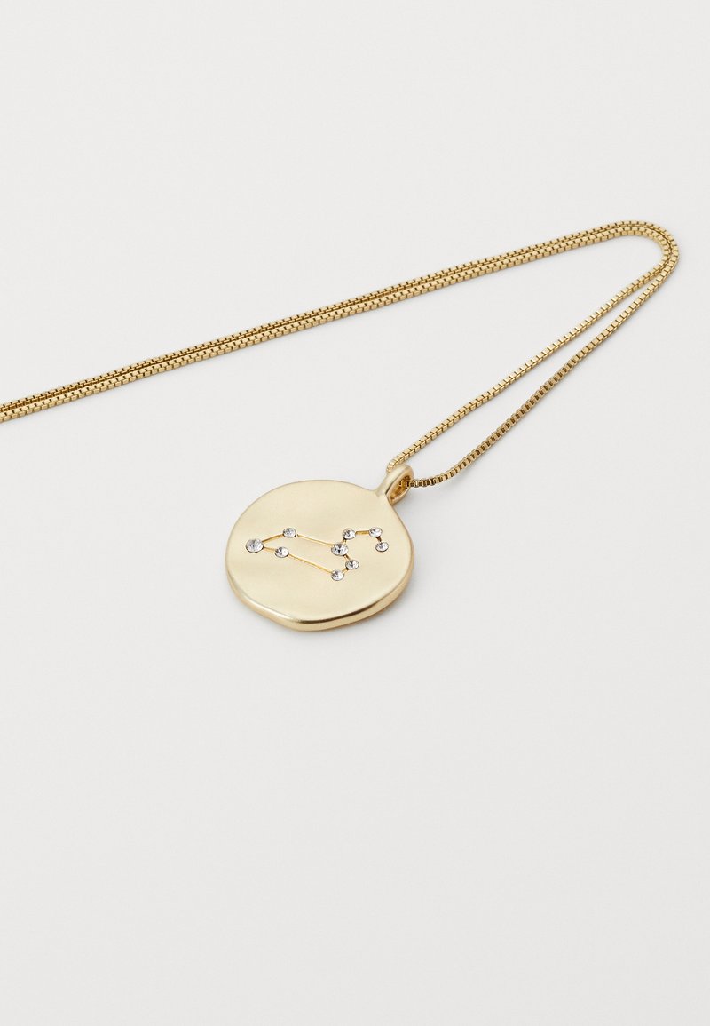 Collar de oro con un colgante redondo que presenta un patrón de constelaciones destacado por pequeños cristales claros sobre un fondo blanco liso.