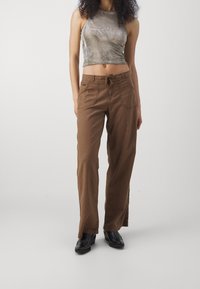 Bruna, löst sittande byxor med dragsko i midjan och sidfickor, ihop med en grå, åtsittande, kort topp. Svarta skor fullbordar looken.