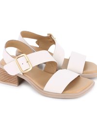 Sandalias de tacón blancas con dos correas anchas y detalle de hebilla lateral. Hechas de cuero suave, con un tacón de bloque con textura de madera natural.