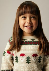 Maglione lavorato a maglia con una base color crema, motivi festivi verdi e rossi che includono volti di Babbo Natale e alberi di Natale, con scollatura rotonda.