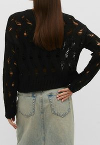 Zwarte gebreide trui met een brede halslijn en opengewerkt patroon. Gecombineerd met een lichtblauwe denim rok met achterzakken.