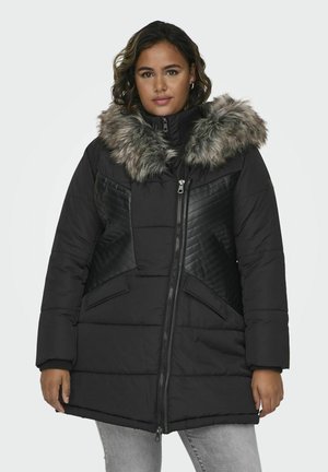 Doudoune noire avec capuche en fausse fourrure, design rembourré, accents en cuir texturé et fermeture éclair à l'avant. Dispose de grandes poches latérales et d'un ourlet légèrement évasé.