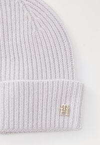 Chapeau tricoté gris clair avec une texture côtelée et un revers, présentant un accent de logo doré sur le côté.