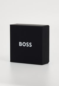Svart rektangulær boks med en glatt tekstur, med ordet "BOSS" i stor, hvit sans-serif-font på fronten.