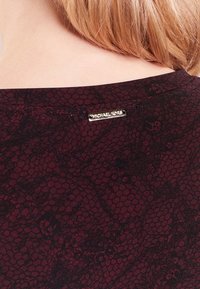 Bordeaux top s krajkovým vzorem, se zlatou visačkou "Michael Kors" na zadní části výstřihu. Měkká textura, přiléhavý střih.