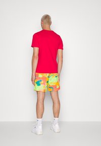 Red short-sleeve T-shirt paired with colorful, tie-dye shorts featuring hues of yellow, pink, green, and blue. Sneakers complete the outfit.