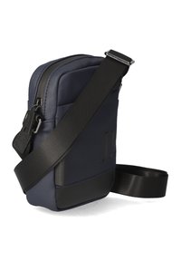 Marinblå nylon crossbody-väska med texturerad yta, svart syntetisk botten, justerbar rem och djärvt präglad logotypdetalj på framsidan.