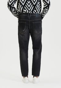 Zwarte denim jeans met een iets losse pasvorm, voorzien van achterzakken en versleten details, gecombineerd met witte sneakers.