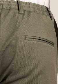Green textured fabric pants with a gathered waistband and a single welt pocket on the back, showcasing a minimalistic design.