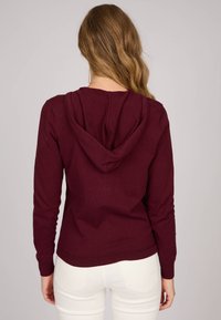 Sweat à capuche bordeaux avec une poche avant, des manches longues et un cordon de serrage ajustable. Tissu en maille texturée ; coupe légèrement ajustée.