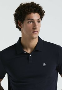 Polo bleu marine en tissu texturé, avec un col classique, des manches courtes et un petit logo brodé sur la poitrine.