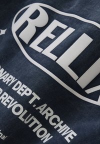 Marineblauwe katoenen T-shirt met een groot wit grafisch tekst met "RELLI" en kleinere tekst eronder. Zachte textuur, casual ontwerp, schuin perspectief.