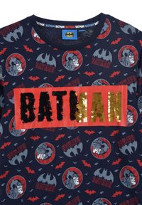 Katoenen t-shirt met een marineblauwe achtergrond, met rode Batman-afbeeldingen en een centrale glanzende sequin "BATMAN" patch in goud en zwart.