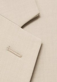 Beiger Stoff mit strukturierter Oberfläche, der zwei gefaltete Abschnitte und ein sichtbares Stichdetail in einer kontrastierenden Fadenfarbe aufweist.
