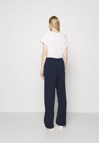 Loose-fitting navy trousers with a textured fabric, paired with a light-colored, short-sleeved top. White footwear completes the look.