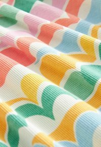 Tissu côtelé coloré avec un motif ondulé en orange, rose, jaune, vert et bleu sur un fond blanc, mettant en valeur une variation de texture.