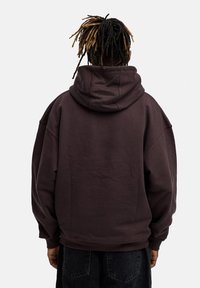 Übergroßer dunkelbrauner Kapuzenpullover mit großer Kapuze, gerippten Bündchen und Saum. Weiche Textur, minimalistisches Design und keine sichtbaren Marken.