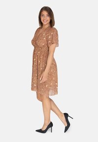 Vestido de estampado floral en marrón con mangas cortas abullonadas, cintura fruncida y falda fluida; combinado con tacones negros de punta. 
