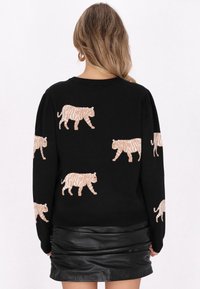 Maglione nero con motivi a tigre beige testurizzati, dotato di maniche lunghe e colletto girocollo classico. Il materiale appare morbido e flessibile.