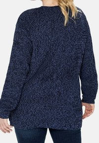 Marinblå stickad tröja med ett strukturellt mönster, långa ärmar och en avslappnad passform, med rund halsringning och en något längre bakdel.