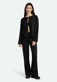 Čierny dvojdielny outfit pozostávajúci z cropped topu so zapínaním v prednej časti a dlhými rukávmi, skombinovaný s nohavicami širokého strihu zdobenými malými nitmi.