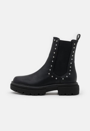 Zwarte chelsea boots van leer, met zilveren studs langs de elastische zijpanelen, een gestructureerde rubberen zool en een trekkoord.