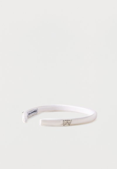 Λευκή σατέν κορδέλα με μικρή τρίγωνη λεπτομέρεια με στρας και ετικέτα με λογότυπο στο εσωτερικό, σε μονόχρωμο φόντο.