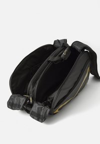 Schwarze Tasche mit zwei Fächern, Reißverschluss sowie verstellbaren Trägern. Enthält goldene Streifen und strapazierfähigen Stoff. Mit Klettverschlussakzenten.