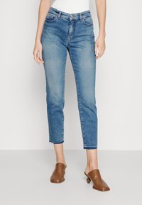 Jeans azul de corte recto y media altura, de lavado claro, con cinco bolsillos, ligero desvanecimiento y tobillos rematados. Combinados con mules marrones.