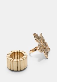 Anello statement in tono oro con design di farfalla adornato da accenti scintillanti, accompagnato da una fascia testurizzata con scanalature verticali.