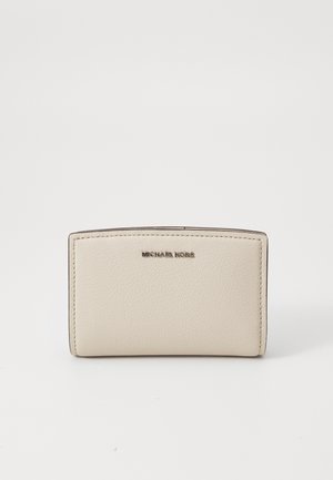 Portofel din piele bej cu o parte superioară curbată, logo-ul "MICHAEL KORS" embosat și cusături vizibile de-a lungul marginilor. Textură netedă, design compact.