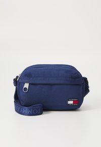 Borsa a tracolla in tessuto blu navy con una consistenza liscia, chiusura con zip e tracolla regolabile, caratterizzata dal logo "TOMMY JEANS" in rosso, bianco e blu.