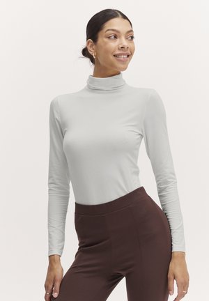 Light gray long-sleeve turtleneck top with a fitted design, paired with high-waisted dark brown pants. Smooth texture, minimal detailing.