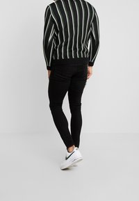 Suéter de punto a rayas blanco y negro con mangas largas, combinado con pantalones ajustados negros y zapatillas blancas con detalles verdes.