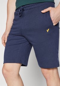 Navy šortky z bavlněného materiálu s páskem na stažení, bočními kapsami a malým žlutým ptáčkem na levé přední nohavic. 