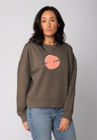 Bruine sweatshirt met een relaxte pasvorm, voorzien van een roze cirkeldesign en zwarte vogels op een draad. Zachte textuur en lange mouwen.