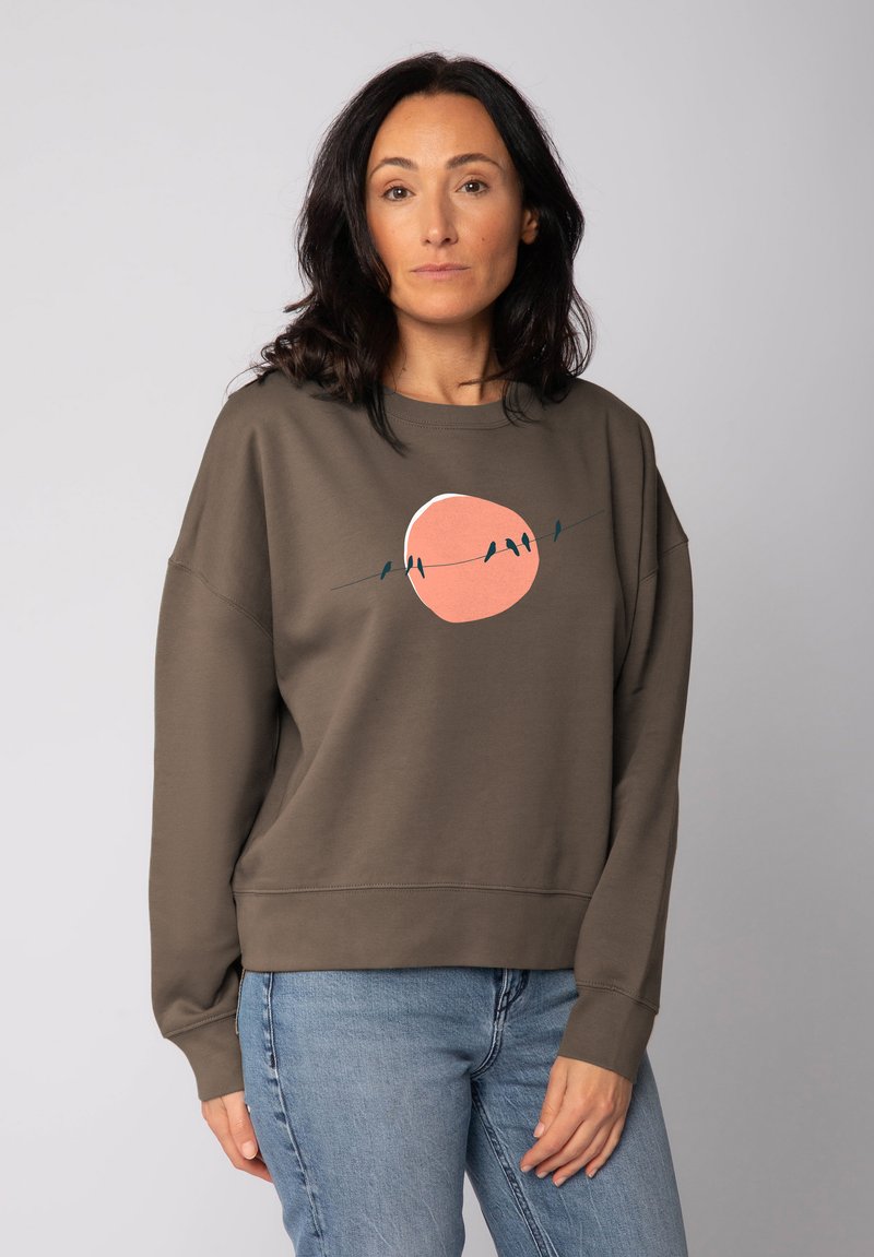 Bruine sweatshirt met een relaxte pasvorm, voorzien van een roze cirkeldesign en zwarte vogels op een draad. Zachte textuur en lange mouwen.