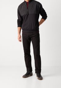 Sudadera negra con panel superior texturizado, media cremallera y puños acanalados, combinada con jeans negros y zapatillas oscuras. Diseño sencillo y moderno.