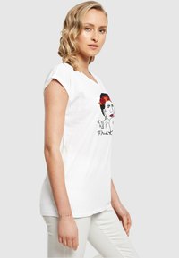 Weißes Baumwoll-T-Shirt mit V-Ausschnitt, das ein grafisches Motiv eines Frauenporträts mit roten Blumen und kräftigen Umrissen zeigt, kurze Ärmel und eine lockere Passform hat.