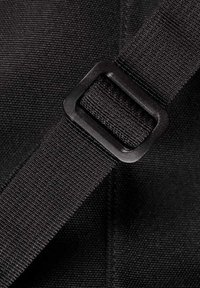 Détail de sangle en nylon noir et de boucle, avec une finition texturée et un régulateur en plastique noir carré le long de la sangle.