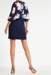 Námořnické šaty s květinovým, lehkým zábalem, krátkými rukávy a přiléhavým střihem, doplněné béžovými lodičkami na vysokém podpatku.