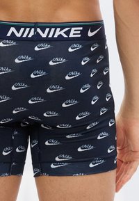 Κοντινό πλάνο ενός ατόμου που φοράει σκούρα μπλε μποξεράκια με λευκά λογότυπα και γραφικά της Nike, εμφανίζοντας την μέση και το πάνω μέρος των μηρών.