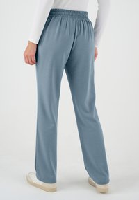 Pantalones de chándal de tela elástica azul claro, con una cintura elástica fruncida, piernas anchas y una textura suave, combinados con zapatillas blancas rotas.