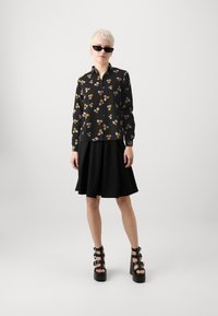 Camisa preta de mangas longas com flores laranja e brancas, combinada com uma saia preta fluida e sandálias pretas de plataforma chunky.