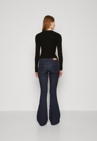Svart ribbet langermet topp kombinert med mørkeblå vide jeans med en beige etikett bak og kontraststingdetaljer.