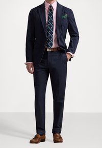 Námořnický blazer s odpovídajícími oblekovými kalhotami, světlá růžová proužkovaná košile, vzorovaná kravata, hnědé kožené boty a zelený kapesníček.